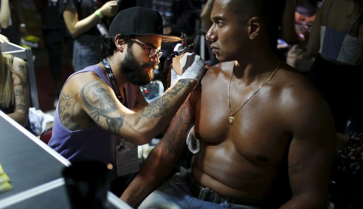 Seorang seniman saat menato seorang pria dibagian bahunya saat Festival Internasional Tattoo Week Rio 2016 ketiga di Rio de Janeiro, Brasil, (22/1/2016). (REUTERS/Pilar Olivares)