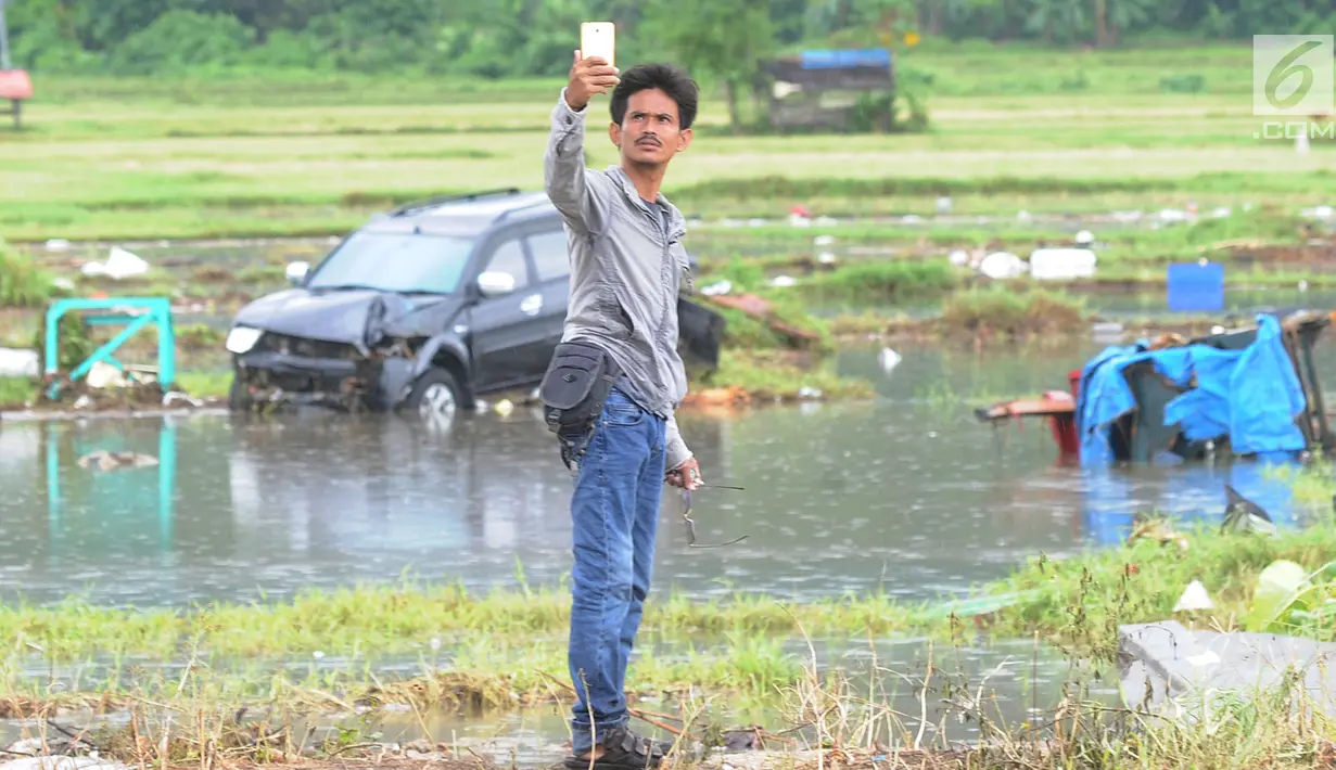 Warga berselfie dengan latar belakang kawasan terdampak bencana tsunami di Carita, Banten, Selasa (25/12). Libur Natal dimanfaatkan warga luar Anyer dan carita untuk menyaksikan langsung terdampak bencana sambil berselfie. (Merdeka.com/Arie Basuki)
