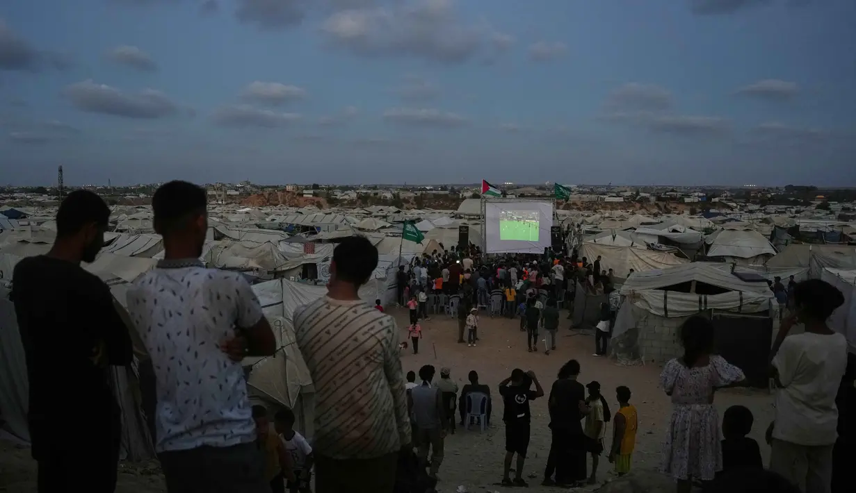 Warga Palestina menyaksikan siaran langsung pertandingan sepak bola Piala Dunia antara Spanyol dan Arab Saudi melalui layer lebar di Nuseirat, Jalur Gaza Tengah, Minggu 21 Juni 2026. (AP Photo/Abdel Kareem Hana)
