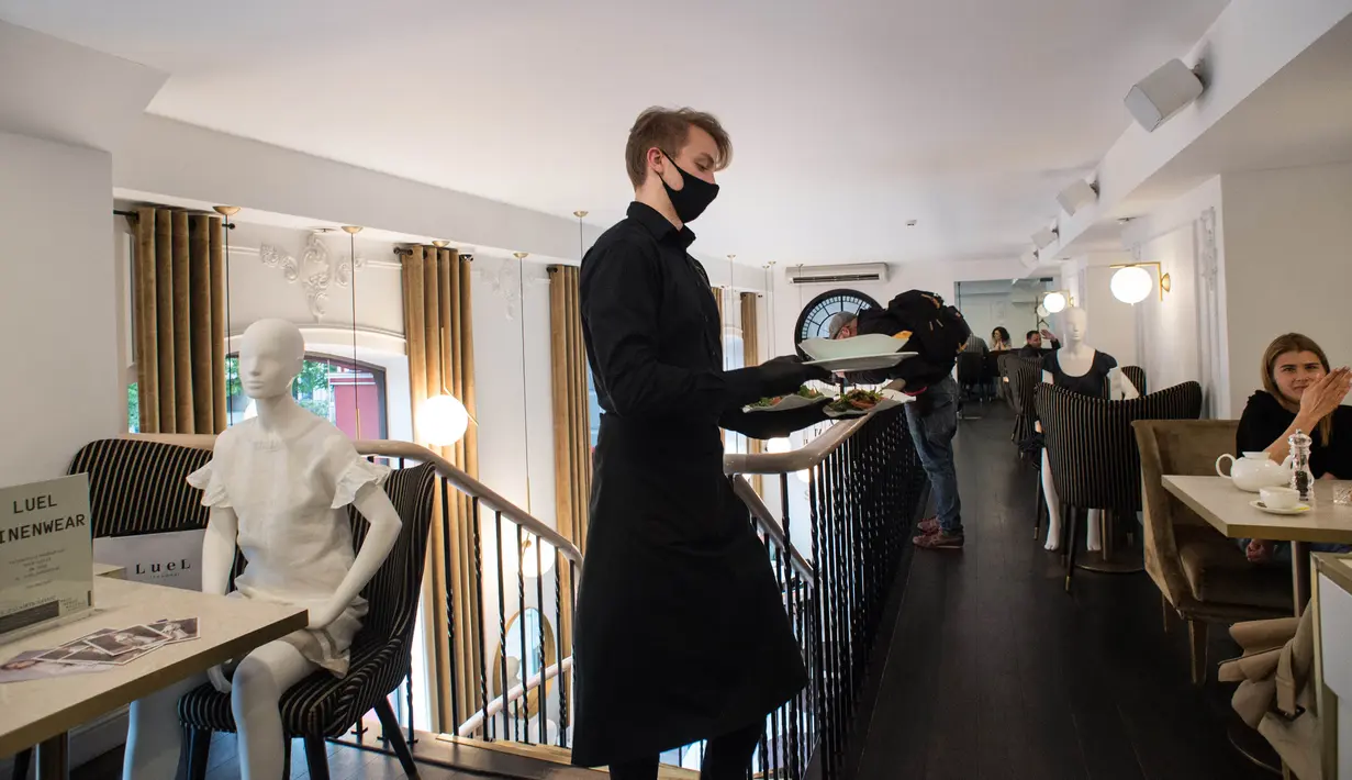 Pelayan berjalan melewati sebuah maneken yang mengenakan busana kreasi desainer lokal di sebuah restoran di Kota Tua Vilnius, Lithuania, Kamis (21/5/2020). Sejumlah restoran dan kafe di Lithuania memamerkan koleksi busana karya desainer lokal yang terdampak COVID-19. (Xinhua/Alfredas Pliadis)