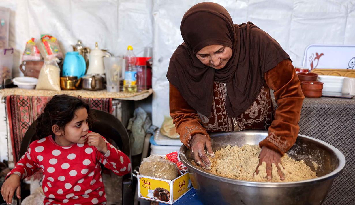 Di setiap negara, roti ini bisa memiliki variasi bentuk dan rasa yang sedikit berbeda. Tampak dalam foto, seorang wanita mengaduk adonan saat menyiapkan biskuit tradisional "kaak" yang berbentuk cincin menjelang Idul Fitri, hari raya yang menandai berakhirnya bulan puasa suci Ramadan, di Kota Gaza pada 16 Maret 2026. (Omar AL-QATTAA/AFP)