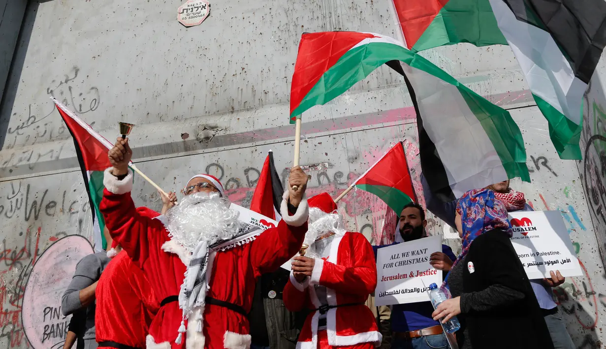 Pengunjuk rasa berkostum sinterklas (Santa Claus) memegang bendera Palestina dalam demonstrasi di Bethlehem, Tepi Barat, 23 Desember 2017. Mereka menentang kebijakan Presiden Donald Trump soal Yerusalem yang diklaim Ibu Kota Israel. (AP/Nasser Shiyoukhi)