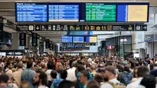 Para penumpang berkumpul di sekitar layar monitor yang menunjukkan jadwal keberangkatan dan kedatangan di stasiun kereta Gare Montparnasse di Paris pada tanggal 26 Juli 2024. (Thibaud MORITZ / AFP)