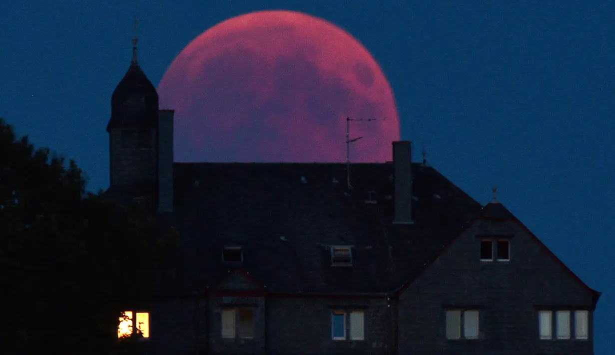 Bulan tampak berwarna merah darah saat terjadinya fenomena gerhana bulan total  di Bernkastel-Kues, Jerman, Jumat (27/7). Gerhana bulan yang terlama pada abad ini dapat disaksikan di seluruh dunia dengan mata telanjang. (Harald Tittel/dpa via AP)