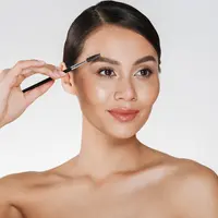 Seorang perempuan sedang merapikan alisnya menggunakan brush make up (Foto Dok: Freepik/ drobotdean).