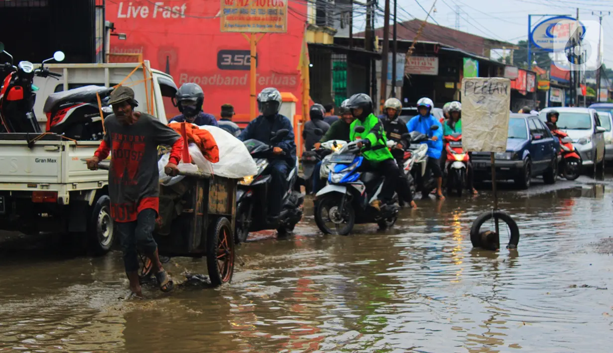 Seorang pria menarik gerobak melintasi jalan berlubang dan tergenang air di Jalan Raya Pabuaran, Citayam, Depok, Rabu (26/2/2020). Kerusakan disebabkan kubangan air yang menggenangi jalan tersebut pada musim hujan  yang melanda Jabodetabek dua bulan terakhir. (merdeka.com/magang/Muhammad Fayyadh)
