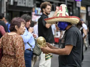 Seorang pedagang kaki lima yang mengenakan topeng gulat tradisional Meksiko menunjukkan suvenir berbentuk piala Piala Dunia kepada pejalan kaki di Mexico City, Senin 8 Juni 2026. (Yuri CORTEZ/AFP)