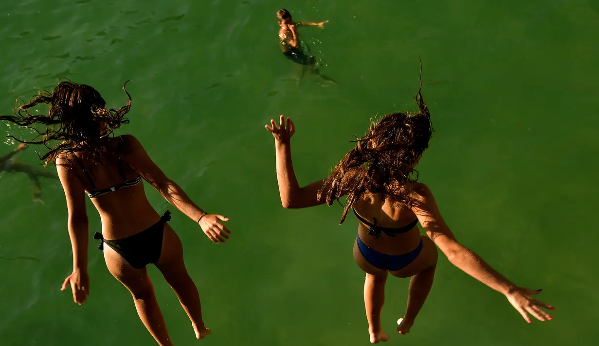 Dua wanita melompat ke air di pantai La Concha saat musim panas di kota basque San Sebastian, Spanyol (3/8).  Udara panas dari Afrika membawa gelombang panas ke Eropa, mendorong peringatan kesehatan tentang debu Sahara Desert. (AP Photo/Alvaro Barrientos)