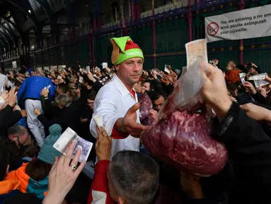 Seorang penjual melelang potongan daging kepada pembeli yang memegang uang selama lelang tahunan menyambut malam Natal di Smithfield Market, London, Selasa (24/12/2019). Dalam tradisi yang hadir sejak 1800-an, calon pembeli bisa menawar harga daging tersebut.  (DANIEL LEAL-OLIVAS / AFP)