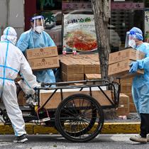 Pekerja yang mengenakan alat pelindung diri menumpuk kotak ke atas gerobak untuk dikirim saat perberlakuan lockdown karena virus corona COVID-19 di Distrik Jing'an, Shanghai, China, Rabu (18/5/2022). (Hector RETAMAL/AFP)