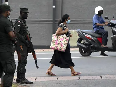 Seorang pejalan kaki melewati tentara yang berjaga di sepanjang jalan di Kolombo pada Sabtu (2/4/2022). Pasukan yang dipersenjatai dengan senapan serbu otomatis dikerahkan di Sri Lanka untuk mengendalikan massa, beberapa jam setelah presiden menyatakan keadaan darurat. (KODIKARA / AFP)