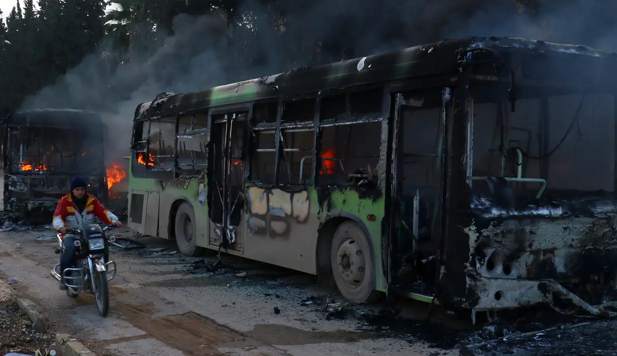 Pengendara motor melewati bus yang diserang dan dibakar saat dalam perjalanan ke al-Foua dan Kefraya di dekat Idlib, Suriah, Minggu (18/12). Bus itu sedianya untuk mengevakuasi warga yang sakit dan terluka di Aleppo timur. (REUTERS/Ammar Abdullah)