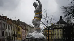 Patung yang dibungkus dengan plastik pelindung di dekat dewan kota di Lviv barat Ukraina, pada 5 Maret 2022. Warga kota Lviv membungkus semua patung yang ada di kota tersebut untuk melindungi warisan sejarahnya dari kerusakan akibat serangan di tengah konflik Rusia-Ukraina. (Daniel LEAL/AFP)