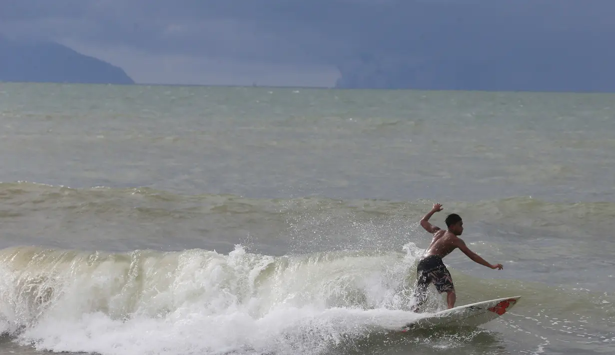 Abu Dzar Al-Ghifari berselancar ketika Gunung Krakatau (kiri) dan Anak Krakatau terlihat di lepas pantai Carita, Banten (26/12). Pemerintah meminta warga menghindari pantai di daerah-daerah tersebut. (AP Photo/Achmad Ibrahim)