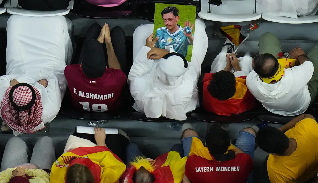 Penonton memegang foto Mesut Ozil di tribun selama pertandingan Spanyol vs Jerman pada laga Grup E Piala Dunia 2022  di Stadion Al Bayt, Kota Al Khor, Senin (28/11/2022) dini hari WIB. Timnas Jerman dan DFB dinilai berani bersuara mengenai isu LGBTQ+, tapi di sisi lain tidak ikut bersuara terhadap isu yang dirasakan Mesut Ozil pada 2018, yang salah satunya adalah rasisme. (AP Photo/Petr David Josek)