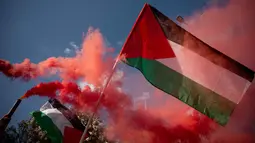 Bendera Palestina terlihat di depan latar belakang asap granat saat demonstrasi menentang pencegatan Armada Global Sumud oleh Angkatan Laut Israel di lepas pantai Siprus di luar Kementerian Luar Negeri, Athena, Yunani, pada 18 Mei 2026. (Aggelos NAKKAS/AFP)