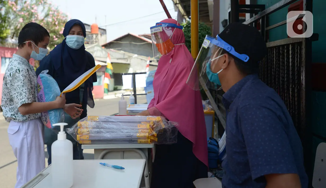 Guru SDIT Ibnu Sina memberikan tugas sekolah secara drive-thru kepada wali murid di Jakarta, Rabu (26/8/2020). Tugas sekolah tersebut dikerjakan oleh siswa dalam satu minggu agar penilaian dan proses belajar mengajar tetap berlangsung. (merdeka.com/Imam Buhori)