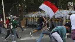 Massa melempar batu ke arah polisi yang membentuk barikade dengan tameng di sekitaran Gedung DPR RI, Jakarta, Senin (30/9/2019). Kericuhan pecah lantaran massa yang kebayakan terdiri dari pelajar tersebut berusaha masuk ke area depan DPR. (Liputan6.com/Angga Yuniar)