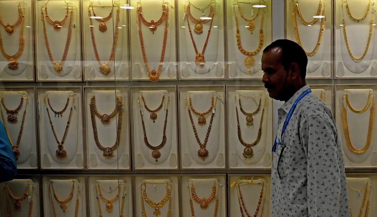 <p>Seorang penjual berjalan melewati kalung emas yang dipajang selama festival Hindu 'Akshaya Tritiya', hari keberuntungan dalam kalender Hindu untuk membeli barang-barang berharga, di ruang pamer perhiasan di Chennai, India, Selasa (3/5/2022). Membeli emas adalah kegiatan yang populer di Akshaya Tritiya, karena ini adalah simbol utama kekayaan dan kemakmuran. (Arun SANKAR / AFP)</p>
