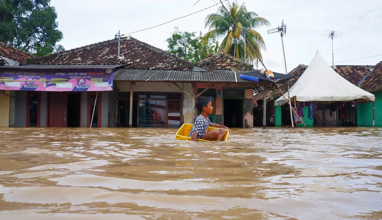 Seorang anak laki-laki menggunakan kotak untuk mengarungi banjir setelah banjir di Serang, Provinsi Banten (1/3/2022).  Berdasarkan data sementara dari Polres Serang Kota, ada 20 titik banjir yang merendam pemukiman warga di Kota Serang. (AFP/Dziki Oktomauliyadi)