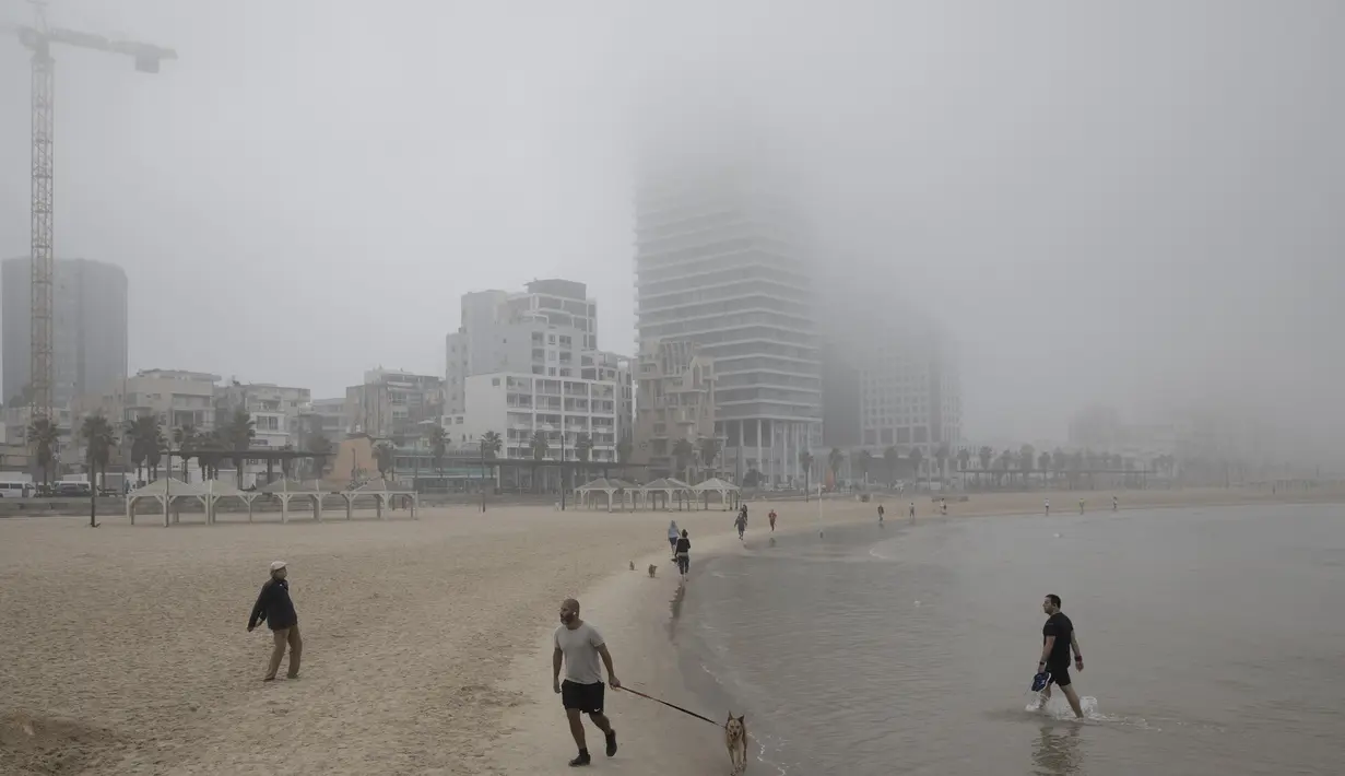 Orang-orang berjalan di pantai saat hari berkabut di Tel Aviv, Israel, Rabu (6/1/2021). Kondisi ini disinyalir dapat mengaburkan jarak pandang dan memperlambat lalu lintas. (AP Photo/Oded Balilty)