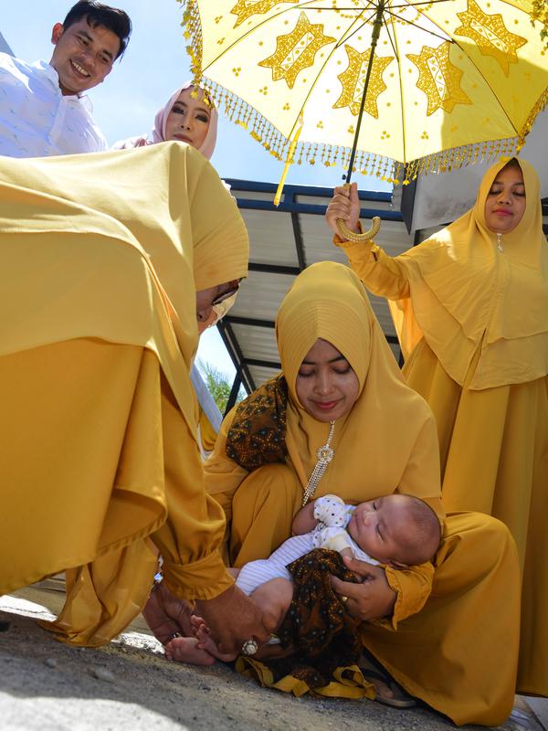 Tokoh adat dan agama menggendong bayi pada ritual 'peutron tanoh aneuk' (turun tanah anak) di Banda Aceh, Aceh, Senin (15/7/2019). Ritual turun tanah anak yang telah menjadi tradisi sakral bagi masyarakat Aceh yang dilaksanakan pada saat bayi berusia 44 hari. (CHAIDEER MAHYUDDIN / AFP)