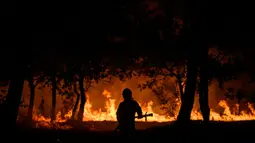 Seorang petugas pemadam kebakaran berdiri di depan api pada kebakaran malam di Saumos di pinggiran barat Bordeaux, Prancis barat daya (12/9/2022). Kebakaran yang berlangsung sejak 12 September 2022 telah menyebar sekitar 1800 hektar vegetasi dan hutan di Saumos dan memaksa evakuasi kota dalam konteks suhu tinggi di Gironde. (AFP/Philippe Lopez)