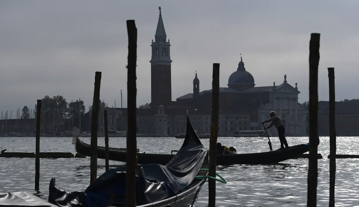 Gondola mengangkut wisatawan yang dekat dengan perairan Riva degli Schiavoni dengan latar gereja San Giorgio Maggiore di Venice (4/11/2019). Di kawasan ini ada pejalan kaki yang ramai meskipun sering penuh sesak di sepanjang tepi pantai, yang terletak di Cekungan St. Mark. (AFP Photo/Miguel Medina)