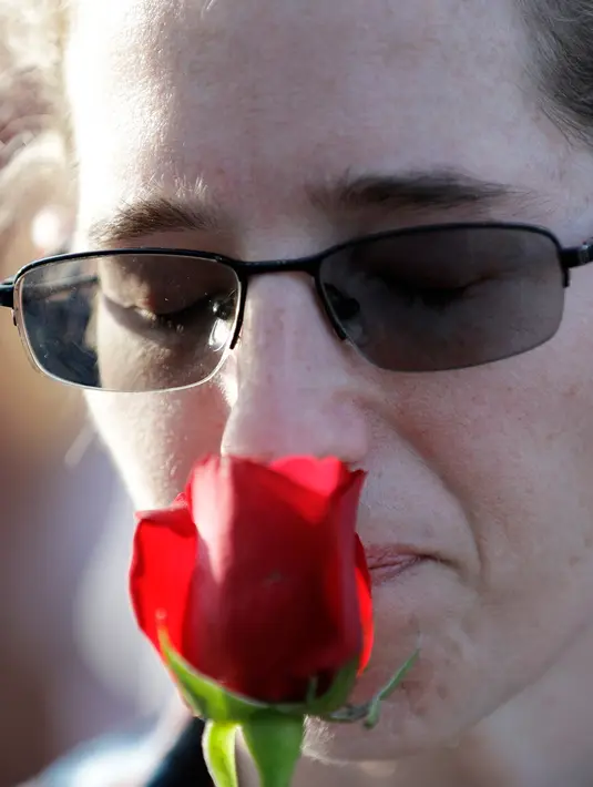 Seorang wanita menempatkan mawar ke wajahnya dalam doa untuk mengenang korban penembakan di sekolah Santa Fe, Texas, Amerika serikat, Jumat (18/5). Pelaku penembakan sudah ditahan dan terancam hukuman mati. (AP Photo/David J. Phillip)