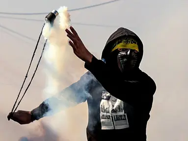 Seorang pemuda Palestina menggunakan ketapel untuk mengembalikan tabung gas air mata ke arah pasukan keamanan Israel saat bentrok pada demonstrasi menentang pengambilalihan tanah oleh Israel dekat pemukiman Yahudi Kedumim di Desa Kfar Qaddum, Tepi Barat, 21 Januari 2022. (JAAFAR ASHTIYEH/AFP)
