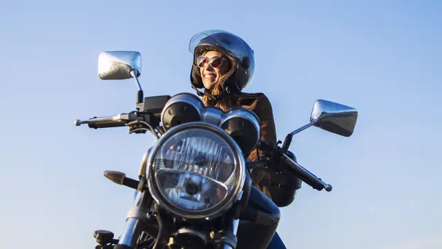 Pengendara motor wanita memakai helm dan mengendarai sepeda motor