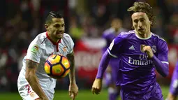 Gelandang Real Madrid, Luka Modric, berebut bola dengan gelandang Sevilla, Vitolo. Selaku tuan rumah, Sevilla sedikit lebih menguasai jalannya laga menurut angka persentase penguasaan bola 54 persen. (AFP/Cristina Quicler)