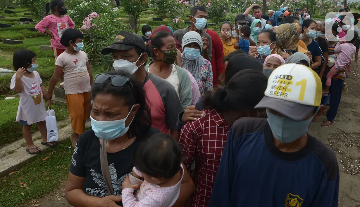 Seorang ibu sambil menggendong anaknya antre pembagian sembako di TPU Malaka, Pondok Kopi, Jakarta, Jumat (4/3/2022). Pembagian sejumlah sembako secara gratis yang diperuntukan bagi kaum duafa ini berupa beras dan minyak goreng. (merdeka.com/Imam Buhori)