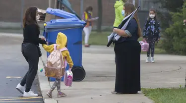 Seorang guru yang memakai masker (kanan) menyapa murid di luar sekolah di Mississauga, Ontario, Kanada  (9/9/2020). Beberapa sekolah di Ontario dibuka kembali pada Rabu (9/9), menawarkan kombinasi kelas tatap muka dan pembelajaran daring (online) bagi para murid. (Xinhua/Zou Zheng)