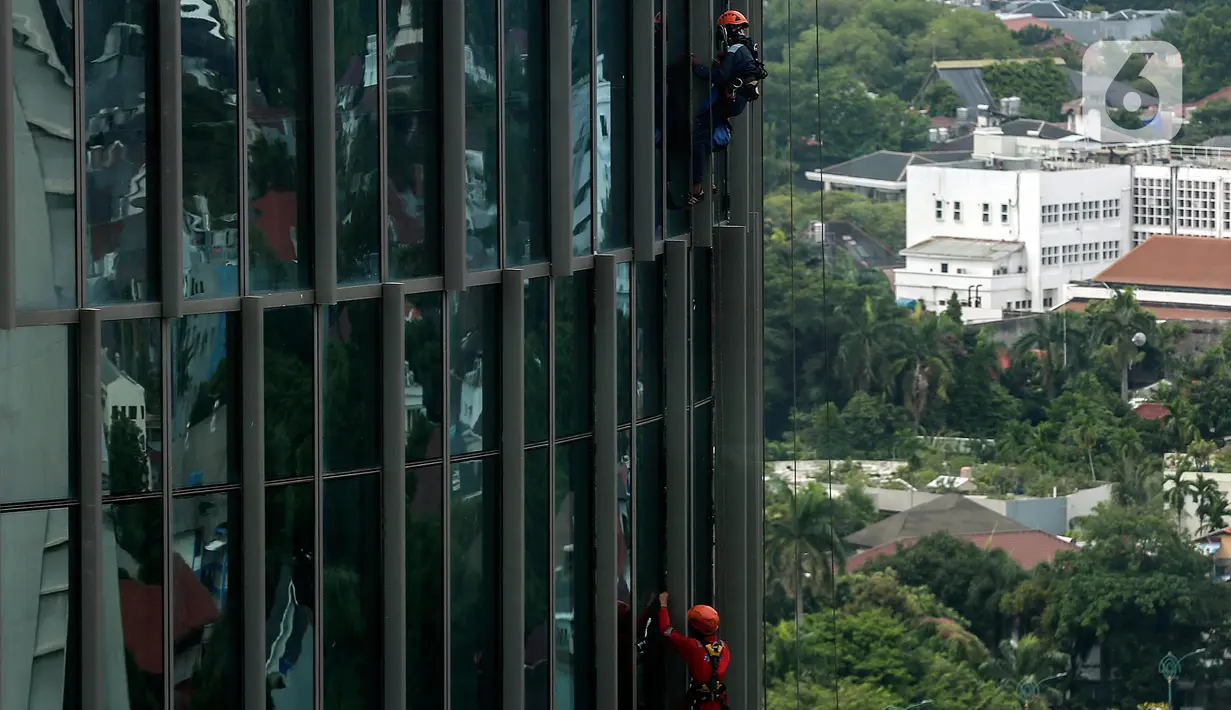 Pekerja saat membersihkan kaca gedung bertingkat di kawasan Kuningan, Jakarta, Minggu (19/12/2021). Pekerja ini harus bergelantungan dengan seutas tali untuk membersihkan dinding-dinding gedung bertingkat yang tingginya kurang lebih mencapai 150 meter. (Liputan6.com/Johan Tallo)