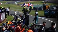 Pembalap Mercedes, Lewis Hamilton membentangkan benedera Inggris saat merayakan kemenangan di Formula 1 GP Inggris 2024 yang berlangsung di Sirkuit Silverstone, Inggris, Minggu (08/07/2024). (AFP/Benjamin Cremel)