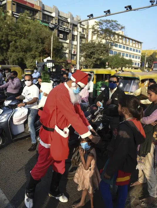 Presiden Angel Foundation dan pekerja sosial, Rufas Christian, yang berpakaian Sinterklas memakaikan masker kepada seorang anak di persimpangan lalu lintas di Ahmedabad, India, Kamis (17/12/2020). Aksi itu sebagai bagian dari kampanye kesadaran melawan penyebaran COVID-19. (SAM PANTHAKY/AFP)