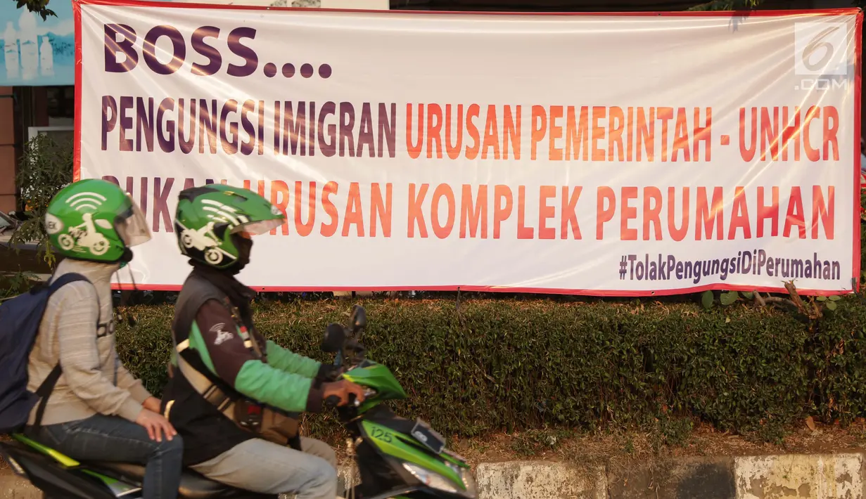 Pengendara motor melintasi spanduk penolakan lokasi penampungan pencari suaka di Kalideres, Jakarta, Selasa (16/7/2019). Sebelumnya, para pencari suaka dari berbagai negara berkonfilk ini tinggal di pinggir jalan dan trotoar di kawasan Kebon Sirih, Jakarta. (Liputan6.com/Helmi Fithriansyah)