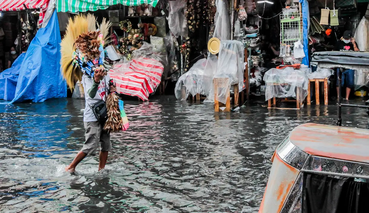 Seorang penjual sapu berjalan melewati banjir di tengah hujan deras yang tiba-tiba mengguyur di sebuah pasar dekorasi Natal di Manila, Filipina (9/12/2020). (Xinhua/Rouelle Umali)