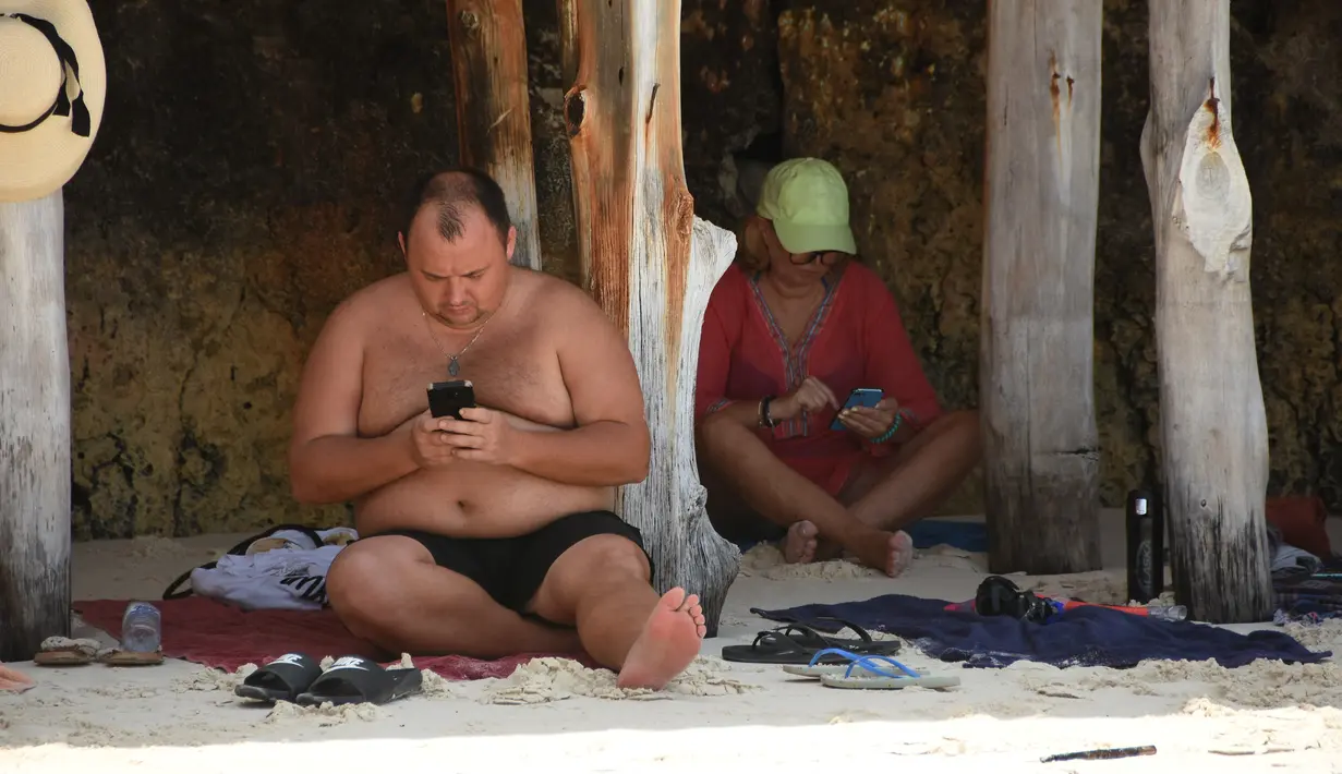 Turis Ukraina memeriksa berita setelah mereka terdampar akibat invasi Rusia ke Ukraina di pantai sebuah hotel di Zanzibar (3/3/2022). Tanzania mengatakan akan menjaga ratusan turis Ukraina yang terdampar di kepulauan Zanzibar di Samudera Hindia. (AFP/Ericky Boniphace)
