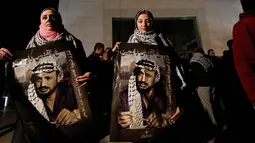 Warga Palestina memegang poster bergambar Yasser Arafat menjelang peringatan 11 tahun wafatnya mantan Presiden Yasser Arafat, di Ramallah, Tepi Barat, Selasa (10/11) malam waktu setempat. (AFP PHOTO / ABBAS Momani)