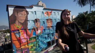 Seniman Brasil, Luna Buschinelli berpose dengan latar belakang mural berjudul 'Contos' di dinding gedung sekolah Rio de Janeiro, (19/6). Karya gadis 19 tahun itu memecahkan rekor dunia sebagai mural terbesar yang dibuat oleh wanita. (AP/Silvia Izquierdo)