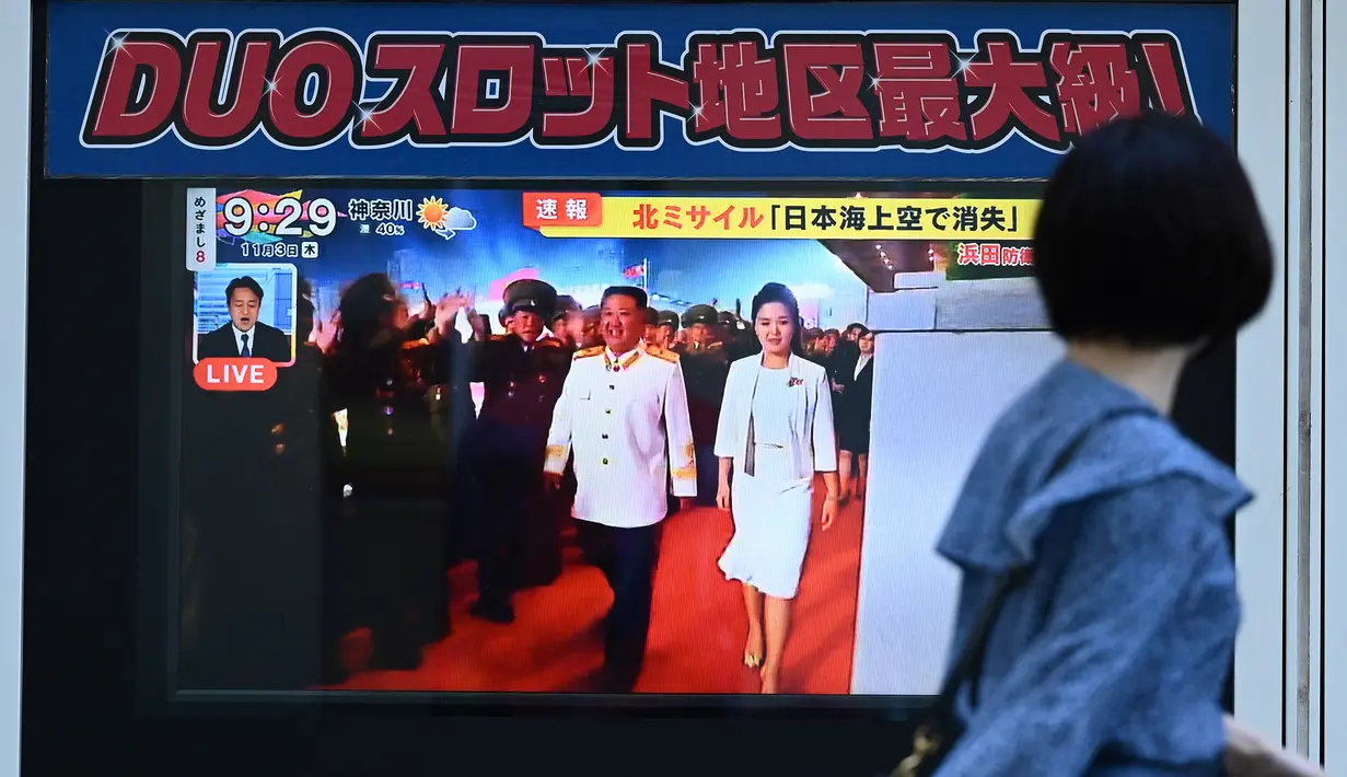 Seorang perempuan melewati layar televisi yang menampilkan laporan berita tentang peluncuran rudal terbaru Korea Utara dengan gambar pemimpin Korea Utara, Kim Jong Un, di sepanjang jalur pejalan kaki di Tokyo, Kamis (3/11/2022). Peluncuran rudal ini dilakukan sehari usai Pyongyang menembakkan lebih dari 20 rudal. (Photo by Richard A. Brooks / AFP)