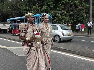 Sepasang pengantin Sri Lanka berjalan menyusuri jalan utama di pusat kota Kandy, 22 September 2017. Pasangan itu membuat kontroversi karena menggunakan sekitar 250 siswa untuk memegang saree atau gaun pengantin wanita India selama pernikahan. (STR/AFP)