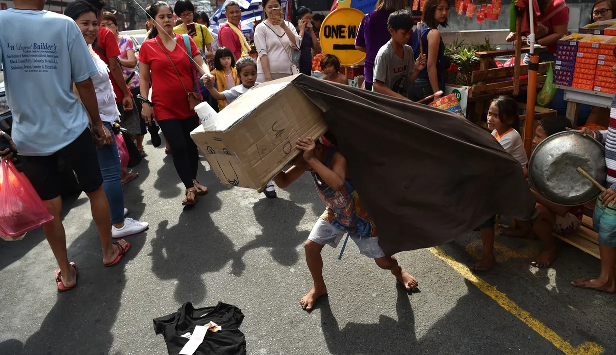 Sejumlah warga menyaksikan Anak-anak melakukan tarian singa dengan kepala singa yang terbuat dari kardus saat menghibur pejalan kaki untuk menyambut Tahun Baru Imlek di Manila (4/2). (AFP Photo/Ted Aljibe)