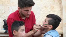 Seorang pria Suriah melukiskan bendera oposisi Suriah di wajah seorang anak selama perayaan Idul Fitri, hari libur Muslim yang dimulai pada akhir bulan puasa Ramadan, di Binnish di provinsi Idlib yang dikuasai pemberontak di barat laut Idlib (26/5/2020). (AFP Photo/Omar Haj Kadour)