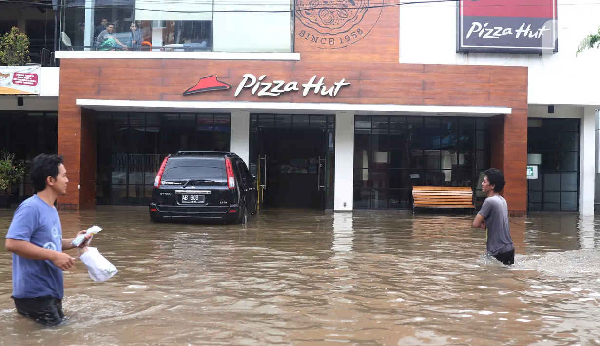 Warga melintas di depan pertokoan yang terendam banjir di Kawasan Bendungan Hilir (Benhil), Jakarta Pusat,  Selasa (25/2/2020). Salah satu wilayah terdampak banjir yakni kawasan Benhil hingga membuat akses jalan untuk sementara terputus.  (Liputan6.com/Angga Yuniar)