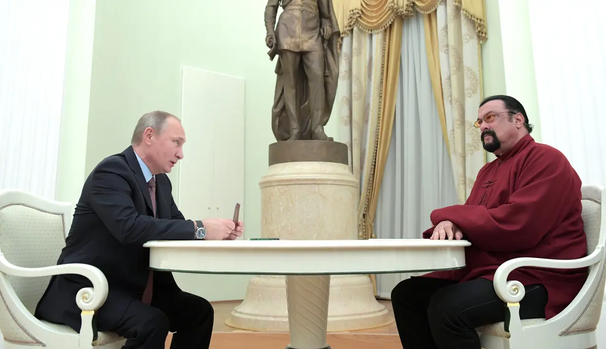 Presiden Rusia Vladimir Putin memegang paspor Rusia sebelum diberikan kepada aktor laga Amerika Serikat, Steven Seagal dalam pertemuannya di Kremlin di Moskow, Rusia, (25/11). (Sputnik/Kremlin/Alexei Druzhinin via REUTERS)