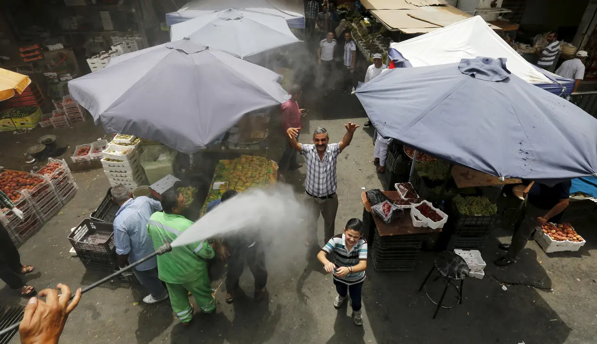 Reaksi sejumlah warga ketika personel dinas Kota Amman menyemprot mereka dengan sprinkler air untuk mengurangi efek dari gelombang panas di Yordania, Senin (3/8/2015). (REUTERS/Muhammad Hamed)