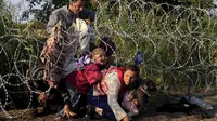 Sejumlah imigran Suriah menyeberangi bawah pagar berduri untuk memasuki negara Hungaria di perbatasan Serbia, 27 Agustus 2015. (REUTERS/Bernadett)
